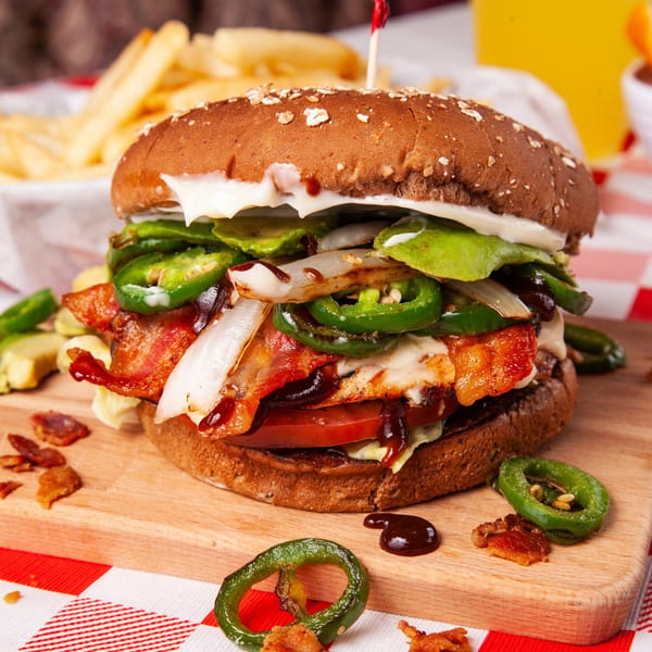A John's Place burger with bacon, jalapeños, onions, and sauce on a wooden board.