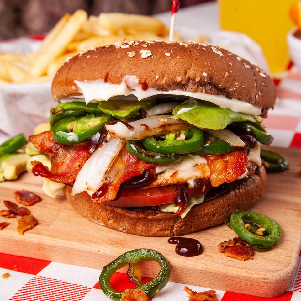 A John's Place burger with bacon, jalapeños, onions, and sauce on a wooden board.