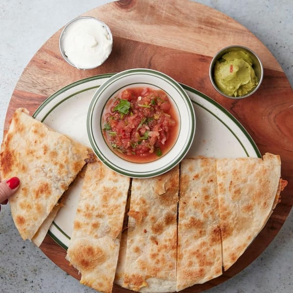 John's Place quesadilla with salsa, guacamole, and sour cream on a wooden board.