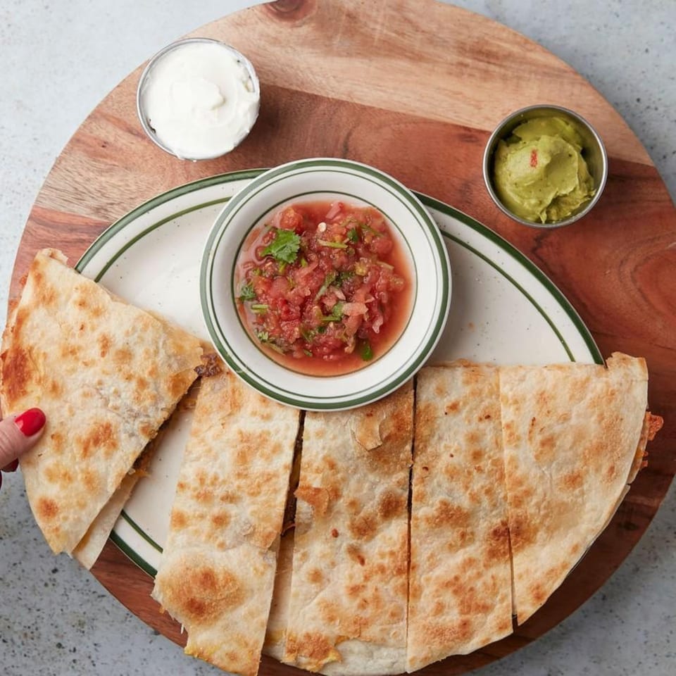 John's Place quesadilla with salsa, guacamole, and sour cream on a wooden board.
