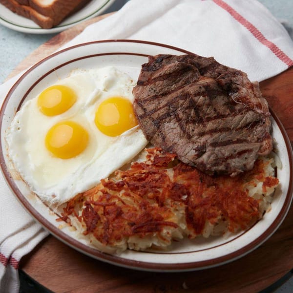 A John's Place breakfast plate with steak, three fried eggs, and crispy hash browns.
