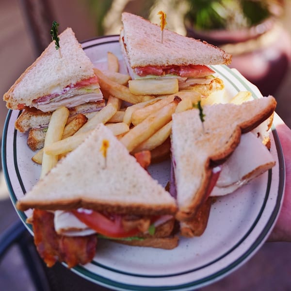 A plate of John's Place club sandwiches, cut into triangles, served with golden french fries.