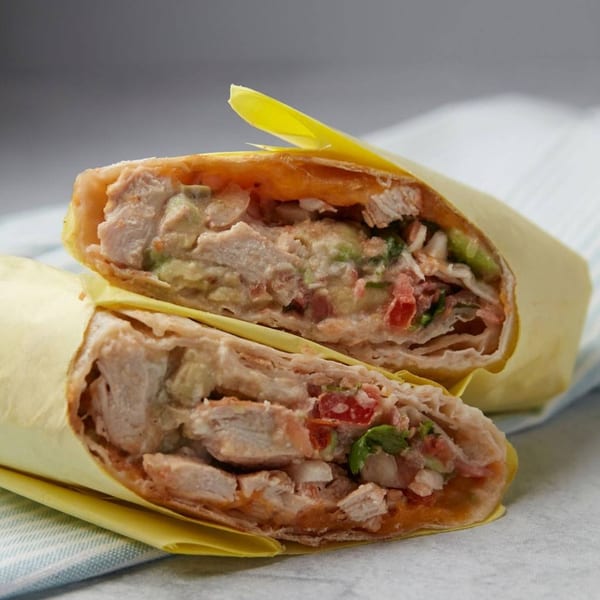 Two halves of a John's Place chicken wrap, filled with meat, avocado, and tomatoes.