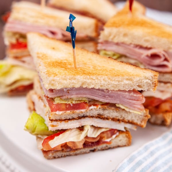 Close-up of a John's Place club sandwich with ham, lettuce, and tomato on toasted bread.