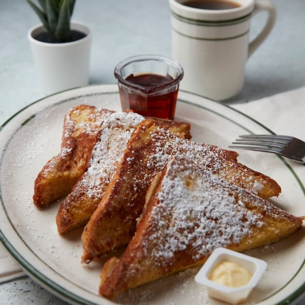 John's Place French toast with powdered sugar, syrup, butter, coffee, and a small plant.