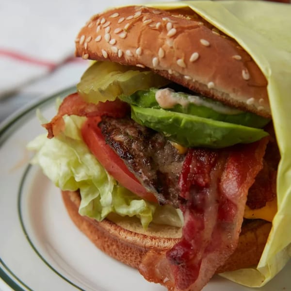 A John's Place burger with bacon, avocado, lettuce, tomato, and pickles on a sesame bun.