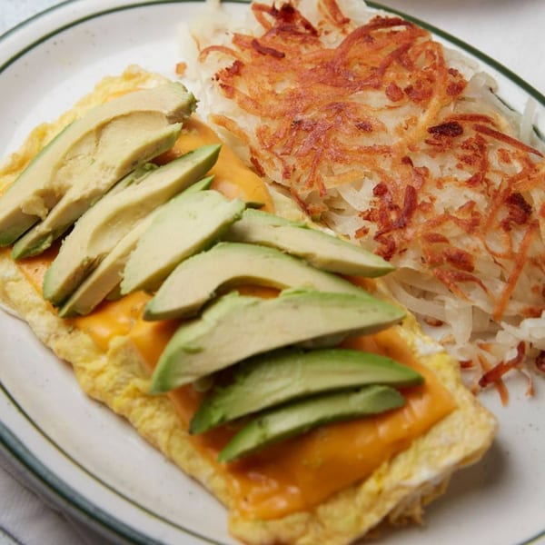 A John's Place omelet with melted cheese and avocado slices, served with crispy hash browns.