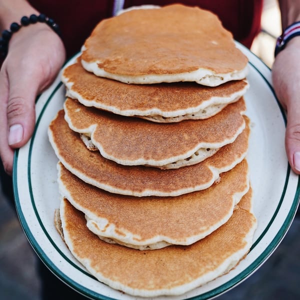 Hands holding a plate piled high with golden-brown pancakes from John's Place.