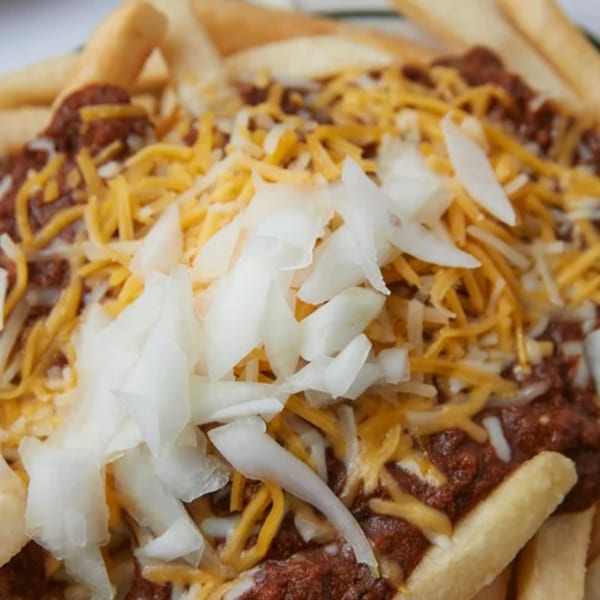 Close-up of John's Place chili cheese fries, topped with shredded cheese and diced onions.